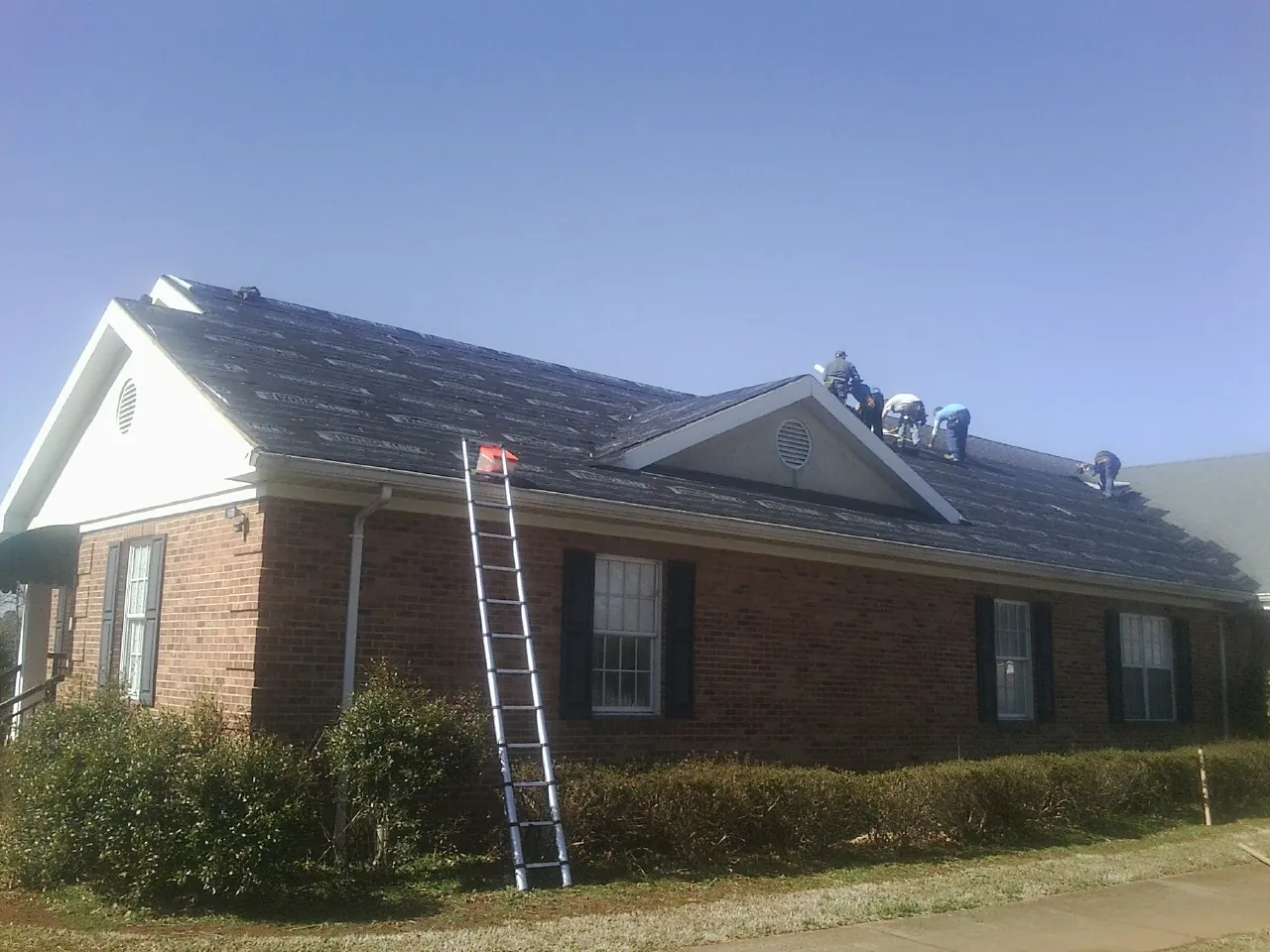 Crew tearing shingles off a brick ranch roof with a ladder set — Emergency Roof Repair work by our crew in Foss