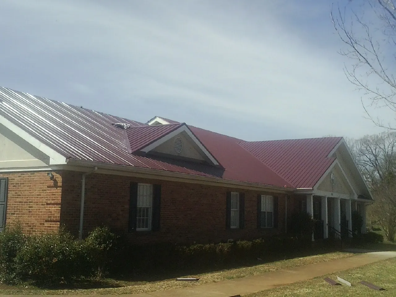 Red metal roof with gabled entries on a long brick building, from a Hail Damage Roof Repair job in Foss