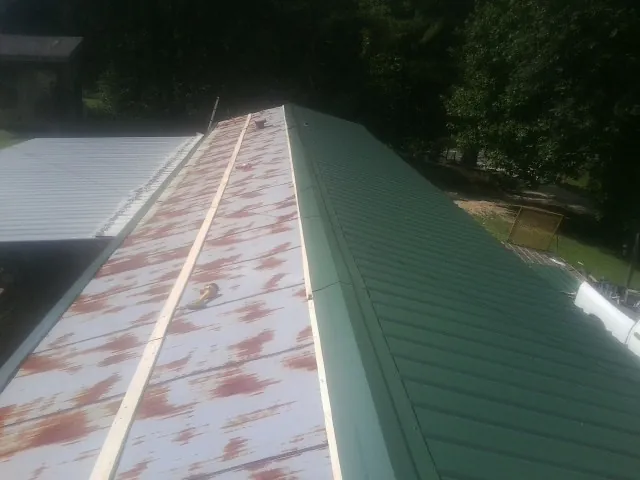 Old rusted panels beside newly installed green metal roofing — Wind Damage Roof Repair by Roofing Brothers in Foss