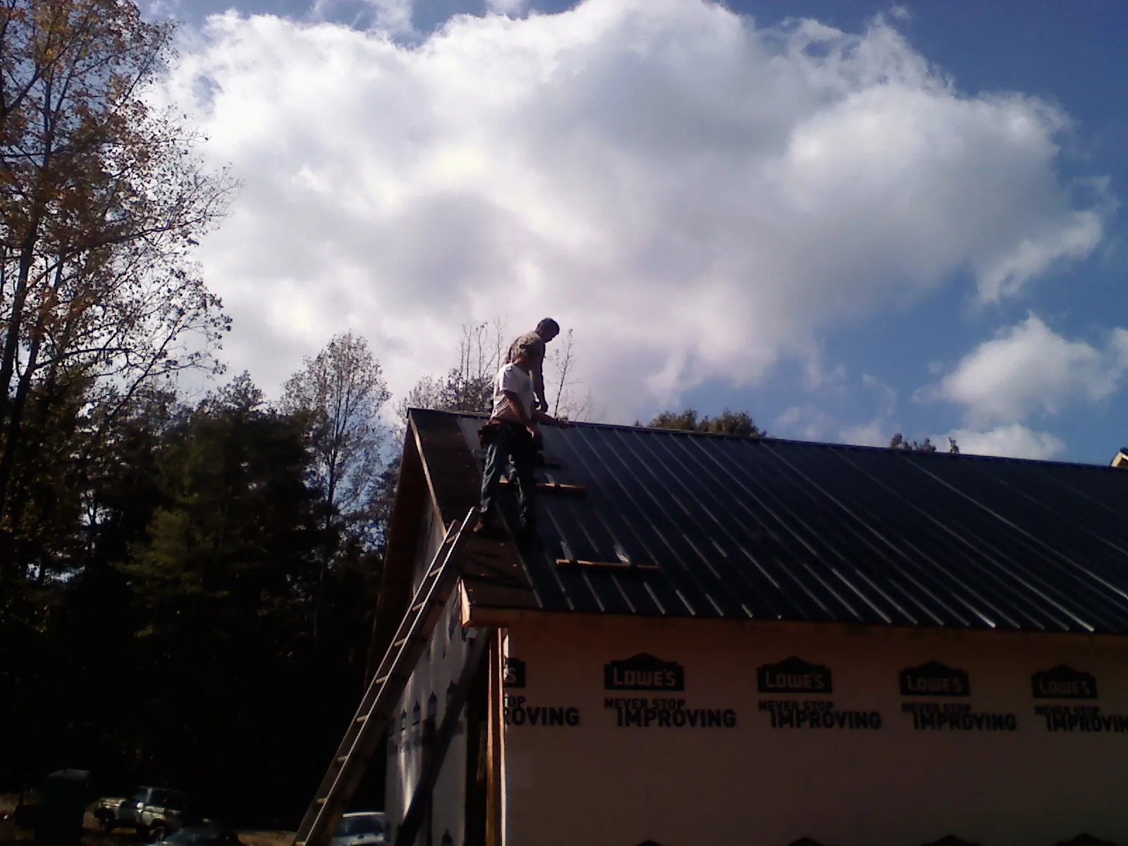 Roofer fastening dark metal panels high against a cloudy sky, from a Roof Inspection job in Foss