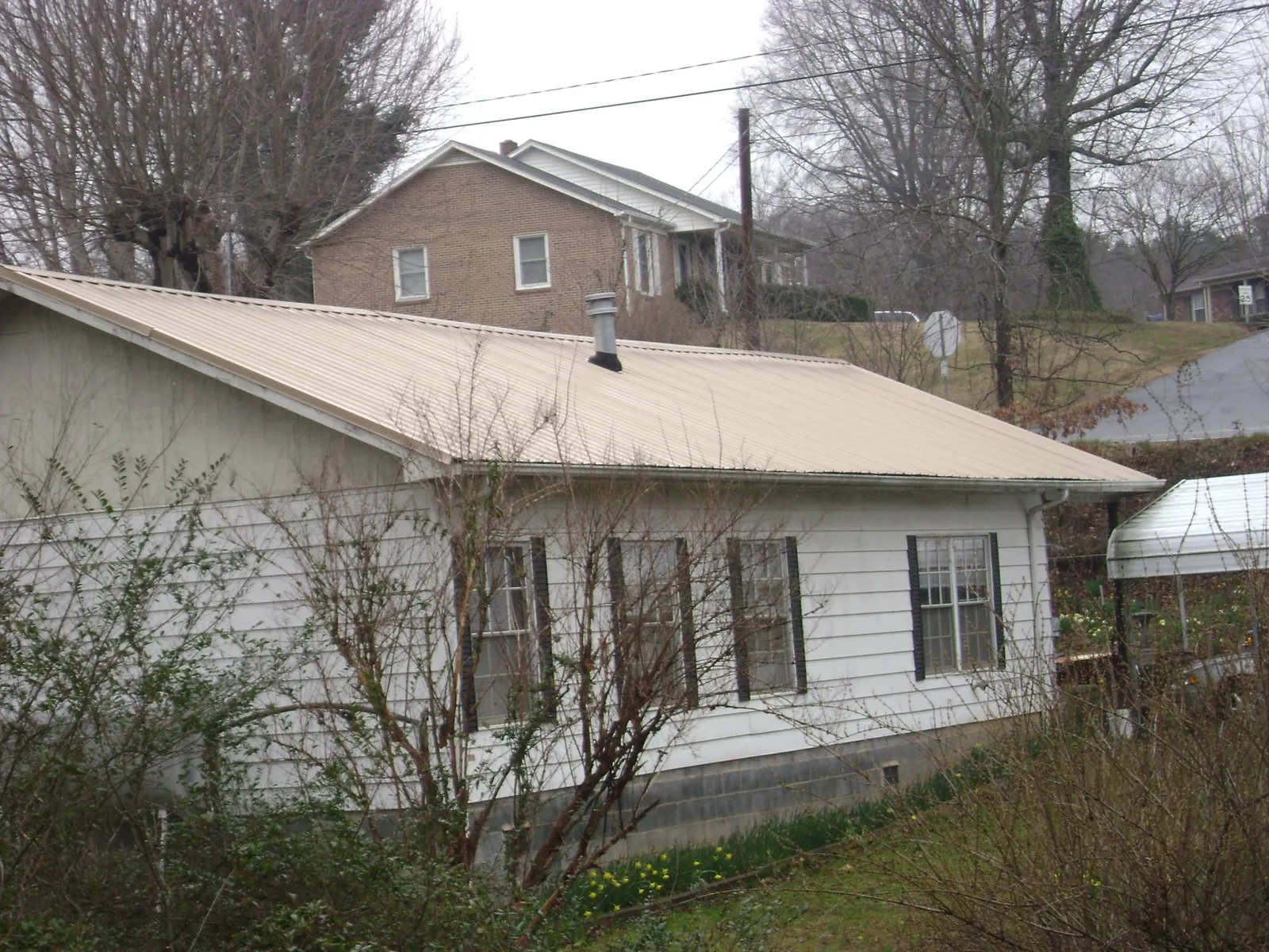 Tan metal roof on a white sided house set into a hillside — Commercial Roofing by Roofing Brothers in Foss